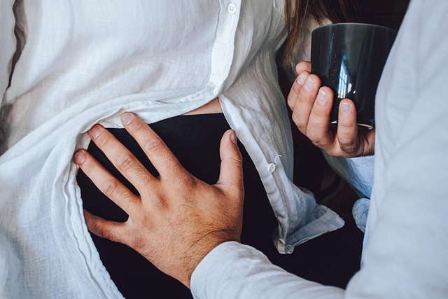 man holding cup of coffee in right hand and holding pregnant woman's belly with left hand