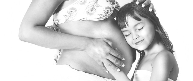 young girl hugging her moms pregnant belly