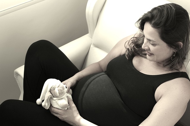 pregnant woman in black dress laying on white couch holding a teddy bear